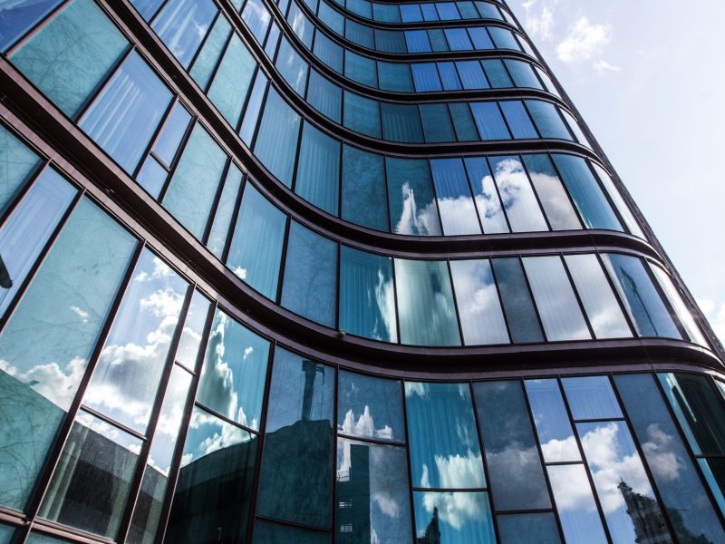 A vertical low angle shot of a high rise building in a glass facade with the reflection of the surrounding buildings